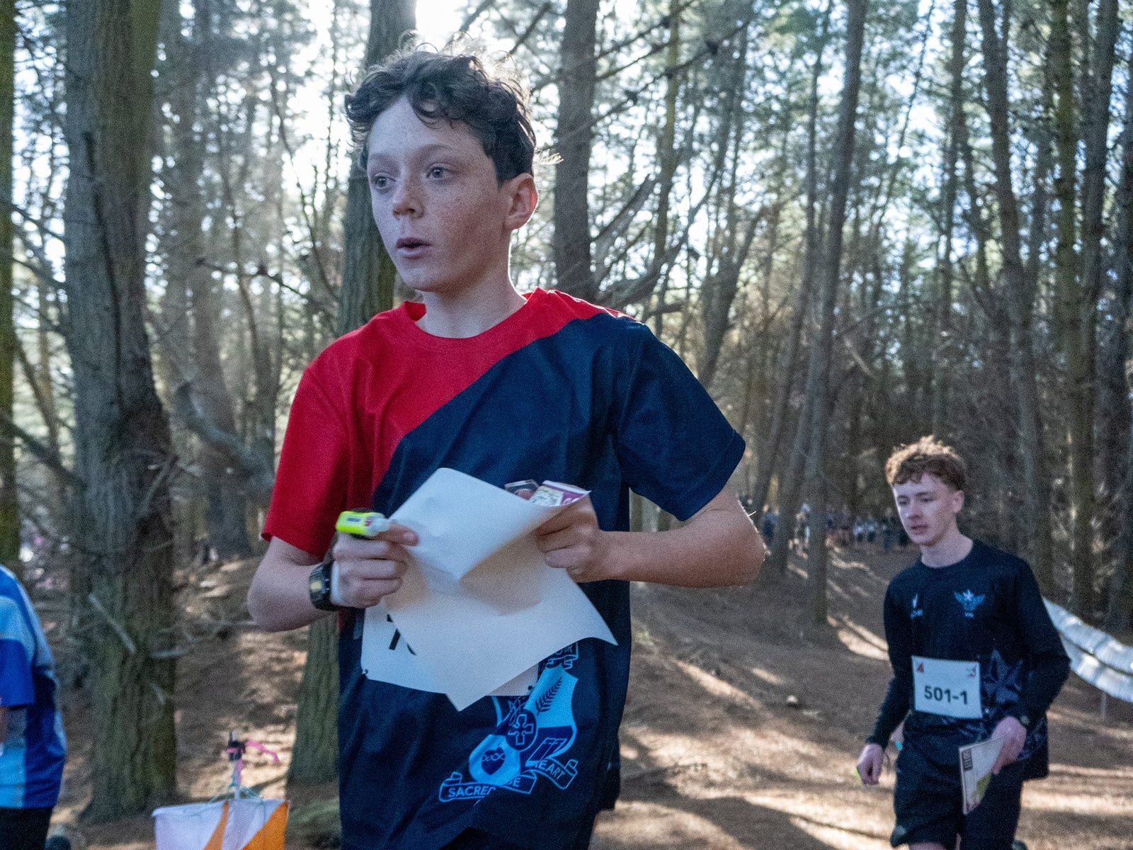 A secondary school orienteer running past a control flag with the map held in one hand