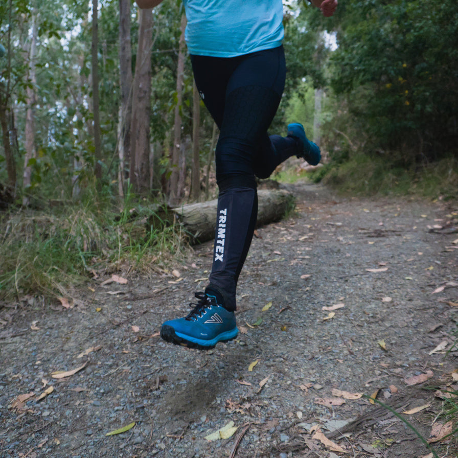 A runner on a forest trail wearing black trimtex gaiters and blue VJ Falcon shoes
