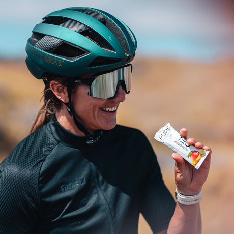 Cyclist in a helmet smiling while holding a PURE Fluid Energy Gel Mango